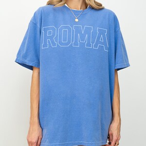 May include: A blue oversized t-shirt with the word "ROMA" printed in white on the front.