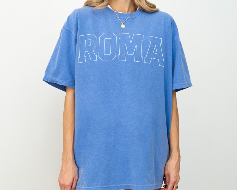 May include: A blue oversized t-shirt with the word "ROMA" printed in white on the front.