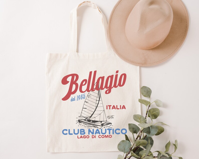 Puede incluir: Una bolsa de lona blanca con un dise&ntilde;o gr&aacute;fico rojo y azul que presenta un velero y el texto "Bellagio dal 1985 ITALIA CLUB NAUTICO LAGO DI COMO".