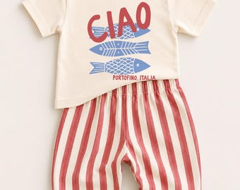 May include: A cream-colored short-sleeve t-shirt featuring the red text CIAO, three blue fish illustrations, and the red text PORTOFINO, ITALIA. Paired with these are pants featuring vertical red and cream stripes with an elasticized waistband.