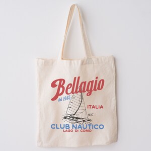 Puede incluir: Una bolsa de lona beige con un dise&ntilde;o gr&aacute;fico rojo y azul. El gr&aacute;fico presenta un velero y el texto "Bellagio dal 1985 ITALIA CLUB NAUTICO LAGO DI COMO".