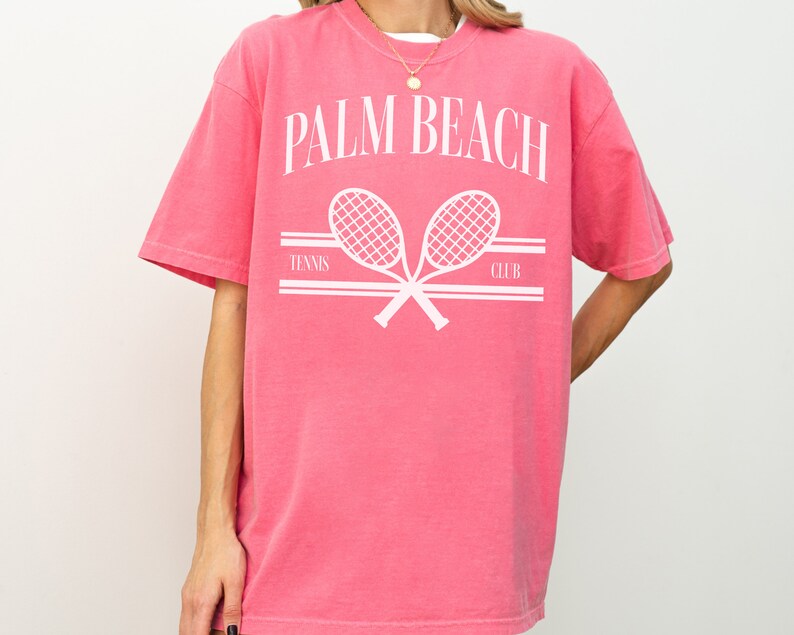 May include: A pink t-shirt with a white graphic of two crossed tennis rackets and the text "PALM BEACH TENNIS CLUB".