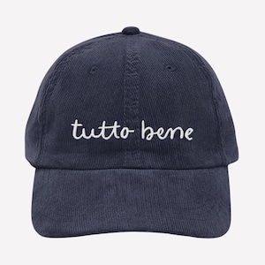 May include: Navy blue corduroy baseball cap with the phrase "tutto bene" embroidered in white script across the front. The cap has a curved brim and an adjustable strap at the back.