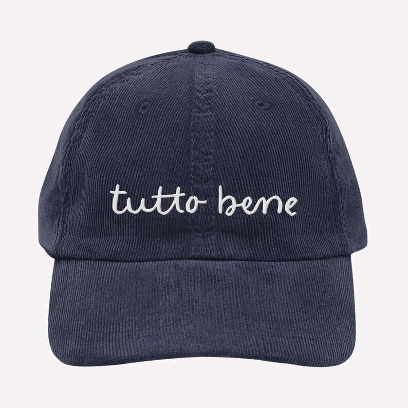 May include: Navy blue corduroy baseball cap with the phrase "tutto bene" embroidered in white script across the front. The cap has a curved brim and an adjustable strap at the back.