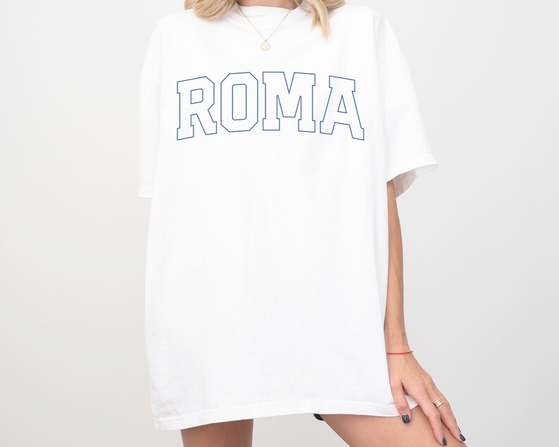 May include: White oversized t-shirt with a blue outline of the word "ROMA" printed on the front.