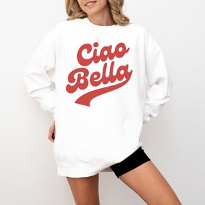 Puede incluir: Sudadera blanca con un gr&aacute;fico rojo de estilo retro que dice "Ciao Bella".