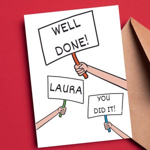 May include: A white card with a cartoon illustration of three hands holding signs. The top sign says "WELL DONE!" The middle sign says "LAURA" and the bottom sign says "YOU DID IT!"