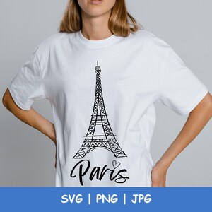 May include: White t-shirt featuring a black graphic of the Eiffel Tower and the word "Paris" in cursive with a heart. The shirt also has the words "SVG | PNG | JPG" in a blue banner at the bottom.