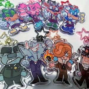 Peut inclure: Une collection de porte-clés de personnages de dessins animés avec divers designs et couleurs. Les porte-clés présentent des personnages avec différentes expressions et tenues, attachés à des fermoirs en forme d'étoile et ronds.