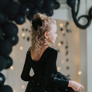 Child in black sparkle tutu bodysuit playing with a star wand under balloon decorations.