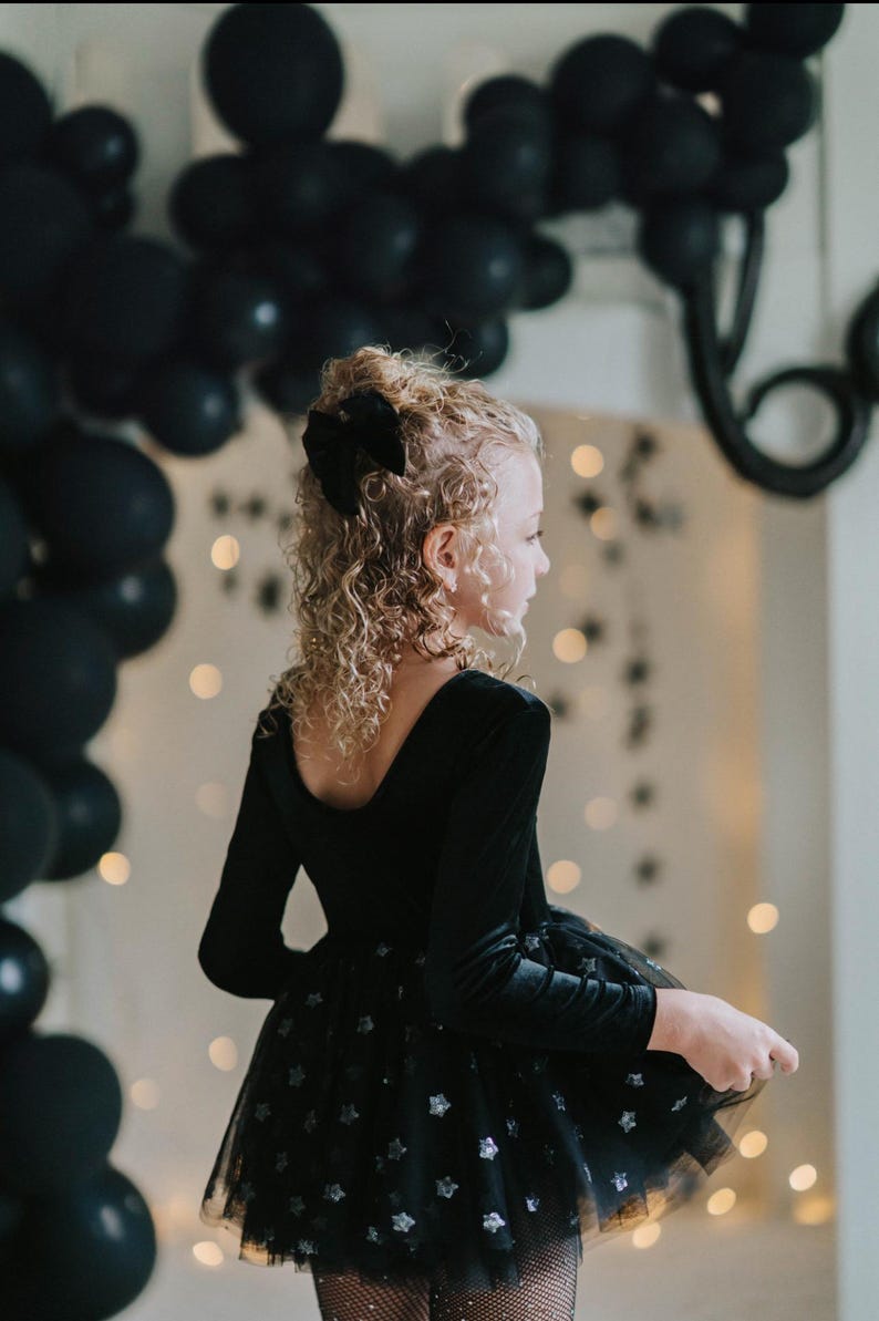 Child in black sparkle tutu bodysuit playing with a star wand under balloon decorations.