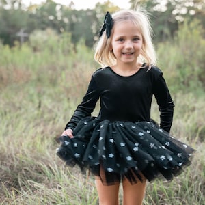 Child spinning in a grassy field wearing a black star-sparkle tutu bodysuit.