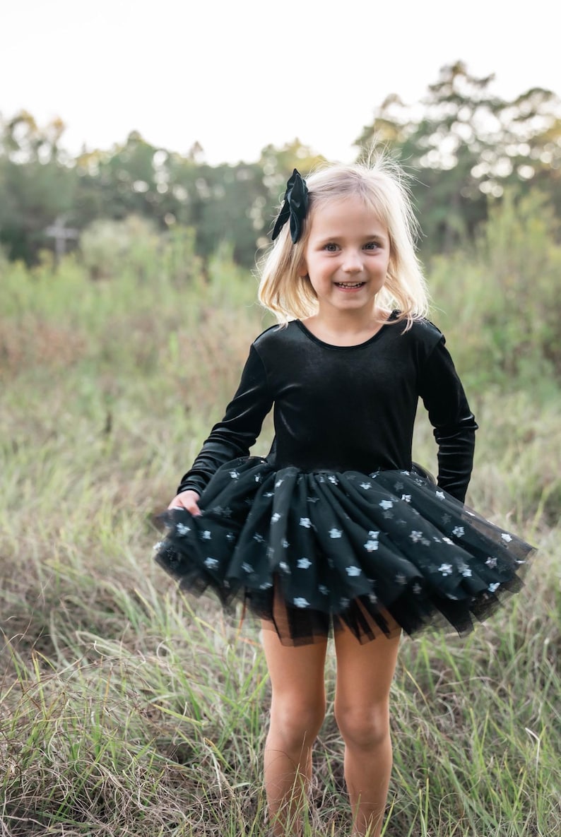 Child spinning in a grassy field wearing a black star-sparkle tutu bodysuit.