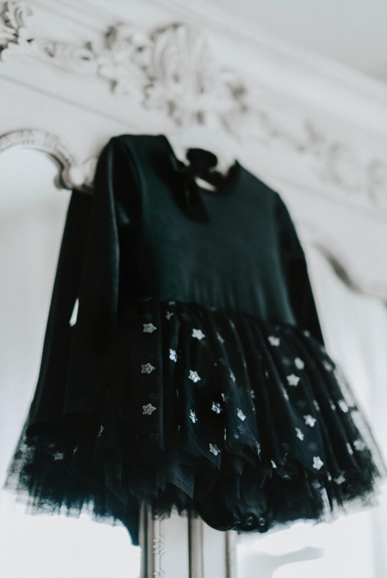 Black velvet tutu bodysuit with starry skirt hanging in soft studio lighting.