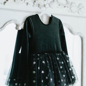 Black velvet long-sleeve tutu bodysuit with starry tulle skirt hanging on vintage mirror.