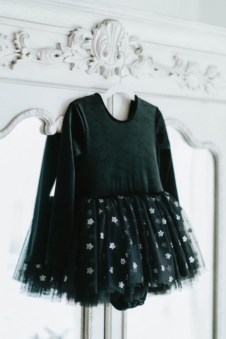 Black velvet long-sleeve tutu bodysuit with starry tulle skirt hanging on vintage mirror.