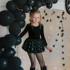 Child modeling black star-sparkle tutu bodysuit in a whimsical party scene.