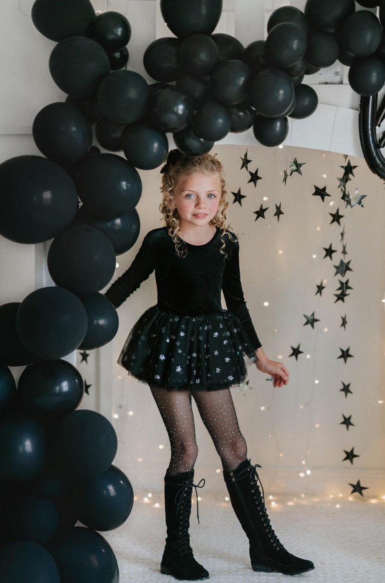 Child modeling black star-sparkle tutu bodysuit in a whimsical party scene.