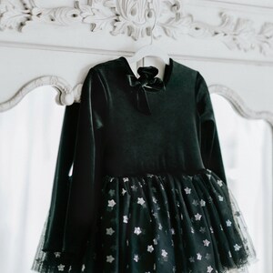 Black velvet tutu bodysuit with matching bow displayed on ornate white dresser.