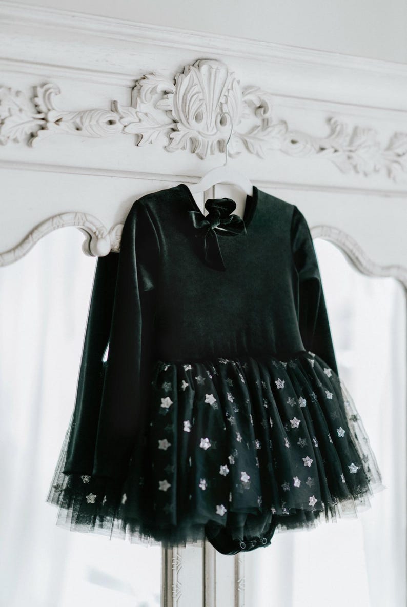 Black velvet tutu bodysuit with matching bow displayed on ornate white dresser.