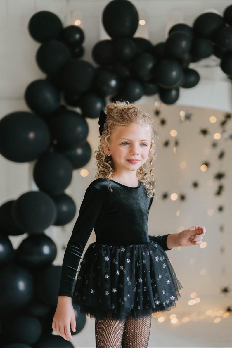 Child posing indoors in a midnight velvet tutu bodysuit with starry backdrop.