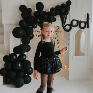 Child posing in a black velvet star-tulle tutu bodysuit under dramatic balloon décor.