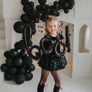 Child wearing black velvet sparkle tutu bodysuit holding Halloween “BOO” balloons.