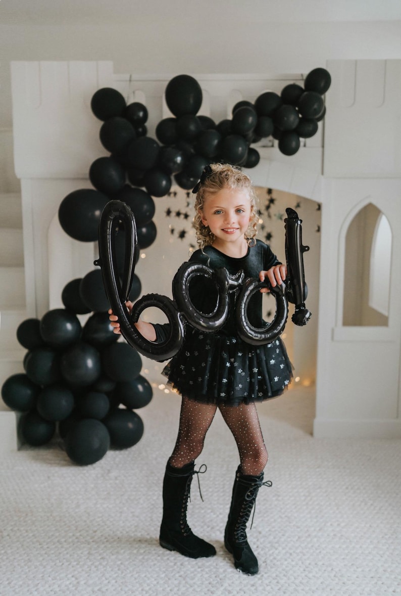 Child wearing black velvet sparkle tutu bodysuit holding Halloween “BOO” balloons.