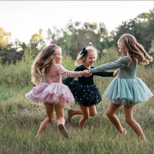 Children twirling outdoors in velvet tutu bodysuits in sage, pink, and black sparkle tulle.