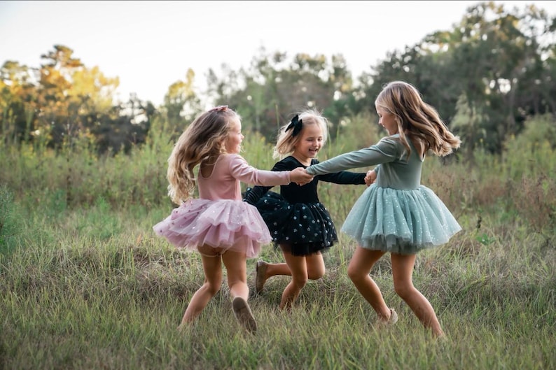 Children twirling outdoors in velvet tutu bodysuits in sage, pink, and black sparkle tulle.
