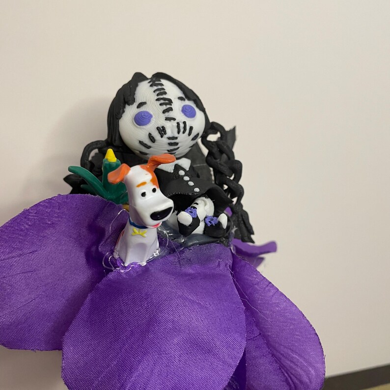May include: A handmade figurine featuring a character with a black and white face, black hair, and a purple flower skirt. A small dog figurine with orange and white markings is also present. The figurine is set against a plain background.