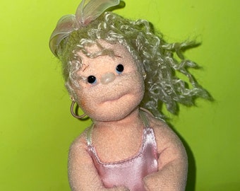 May include: A handmade doll with blonde curly hair, wearing a pink dress and a white bow. The doll has blue eyes and is wearing earrings.