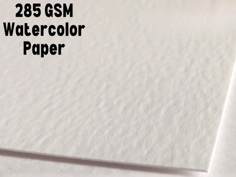 Puede incluir: Primer plano de una hoja de papel de acuarela blanco. El papel tiene una superficie texturizada y el texto "285 GSM Watercolor Paper" est&aacute; impreso en negro en la parte superior.