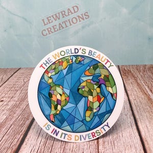 May include: A round sticker with a colorful stained-glass style depiction of the Earth. The continents are composed of various colors, and the background is blue. The text "THE WORLD'S BEAUTY IS IN ITS DIVERSITY" is printed around the edge in rainbow colors.
