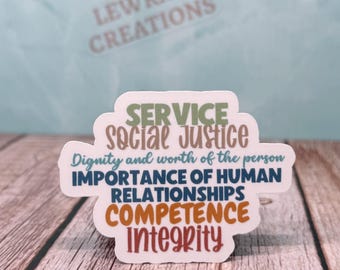 May include: A white sticker with the words "SERVICE", "Social Justice", "IMPORTANCE OF HUMAN RELATIONSHIPS", "COMPETENCE", and "Integrity" in various colors. The sticker also includes the phrase "Dignity and worth of the person". The sticker is on a wooden surface.