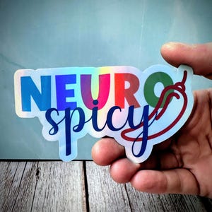 Pu&ograve; includere: Adesivo olografico con le parole "NEURO spicy" in un carattere sfumato arcobaleno. Una grafica di peperoncino rosso &egrave; sul lato destro. L'adesivo &egrave; tenuto da una mano su uno sfondo azzurro.