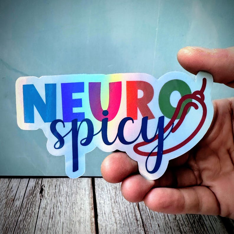 Pu&ograve; includere: Adesivo olografico con le parole "NEURO spicy" in un carattere sfumato arcobaleno. Una grafica di peperoncino rosso &egrave; sul lato destro. L'adesivo &egrave; tenuto da una mano su uno sfondo azzurro.