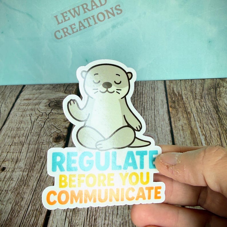 Puede incluir: Una pegatina troquelada que muestra una nutria de dibujos animados de color verde claro sentada en posici&oacute;n de meditaci&oacute;n con los ojos cerrados. Debajo de la nutria, el texto dice REGULATE en azul, BEFORE YOU en amarillo y COMMUNICATE en naranja.