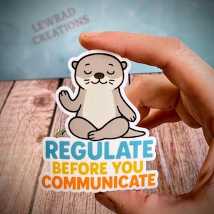 Puede incluir: Una pegatina troquelada que muestra una nutria de dibujos animados de color marr&oacute;n claro sentada en posici&oacute;n de meditaci&oacute;n con las piernas cruzadas y los ojos cerrados. Debajo, el texto dice REGULATE en azul y BEFORE YOU COMMUNICATE en amarillo y naranja.