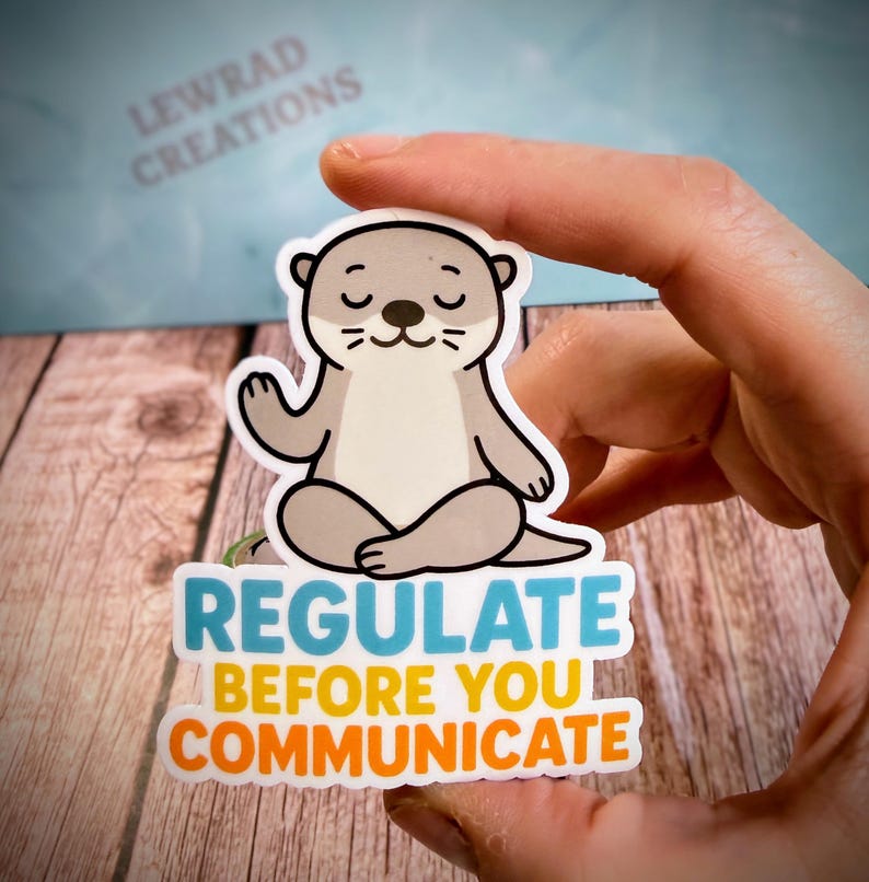 Puede incluir: Una pegatina troquelada que muestra una nutria de dibujos animados de color marr&oacute;n claro sentada en posici&oacute;n de meditaci&oacute;n con las piernas cruzadas y los ojos cerrados. Debajo, el texto dice REGULATE en azul y BEFORE YOU COMMUNICATE en amarillo y naranja.