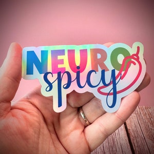 Pu&ograve; includere: Adesivo olografico con le parole "NEURO spicy" in lettere colorate e un'illustrazione di peperoncino rosso. L'adesivo &egrave; tenuto in mano su uno sfondo rosa.
