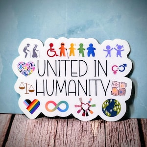 May include: A white sticker with the words "UNITED IN HUMANITY" in black. The sticker features colorful illustrations of people, symbols of equality, and a rainbow heart. The background is a light blue.