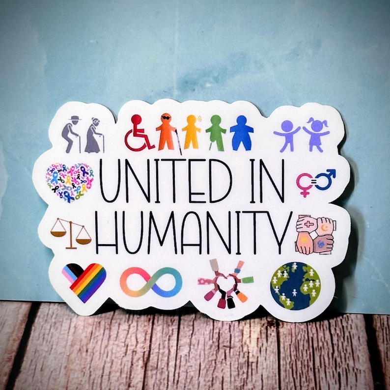May include: A white sticker with the words "UNITED IN HUMANITY" in black. The sticker features colorful illustrations of people, symbols of equality, and a rainbow heart. The background is a light blue.