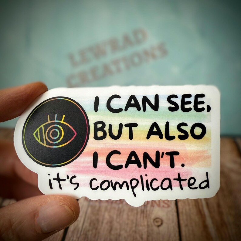May include: A white sticker with the text "I CAN SEE, BUT ALSO I CAN'T. it's complicated." The sticker has a black circle with an eye design and a rainbow gradient background.
