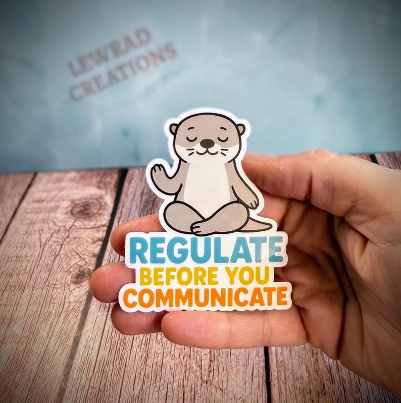 Puede incluir: Una pegatina troquelada que muestra una nutria de dibujos animados de color marr&oacute;n claro sentada en posici&oacute;n de meditaci&oacute;n con los ojos cerrados. Debajo, el texto dice REGULATE en azul, BEFORE YOU en amarillo y COMMUNICATE en naranja, en negrita.