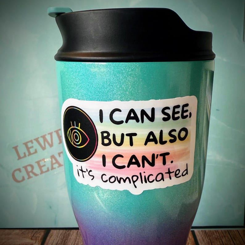 May include: A teal and purple travel mug with a black lid and a white sticker. The sticker has the text "I CAN SEE, BUT ALSO I CAN'T. it's complicated" with a rainbow eye graphic.