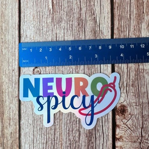 Pu&ograve; includere: Un adesivo olografico con le parole "NEURO spicy" in un font colorato, con una grafica di peperoncino. L'adesivo &egrave; lungo circa 10 cm.