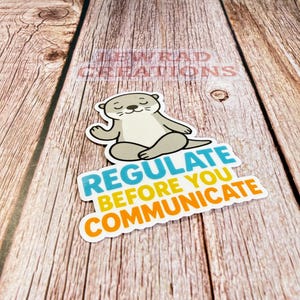 Puede incluir: Una pegatina troquelada que muestra una nutria de dibujos animados de color marr&oacute;n claro sentada en posici&oacute;n de loto con los ojos cerrados. Debajo de la nutria, el texto dice REGULATE en azul, BEFORE YOU en amarillo y COMMUNICATE en naranja.