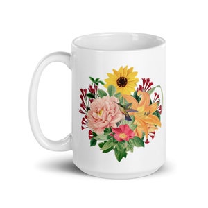May include: White ceramic mug with a floral design featuring a sunflower, pink peonies, orange lilies, red flowers, and a hummingbird.