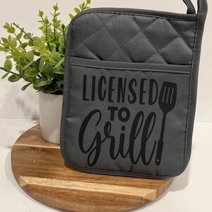 May include: Gray quilted oven mitt with black text that reads "Licensed to Grill!" and a black spatula graphic.